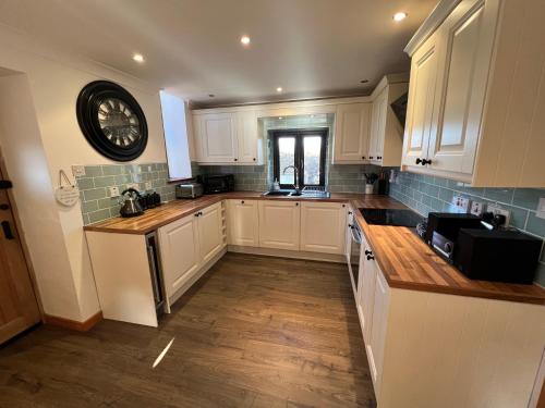 a kitchen with white cabinets and a clock on the wall at 3 Bed Detached Cottage- Log Burner Mountain Views in Beaumaris