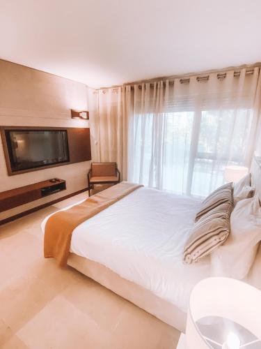 a bedroom with a large white bed and a tv at Troia - Paraíso a um passo de Lisboa in Troia