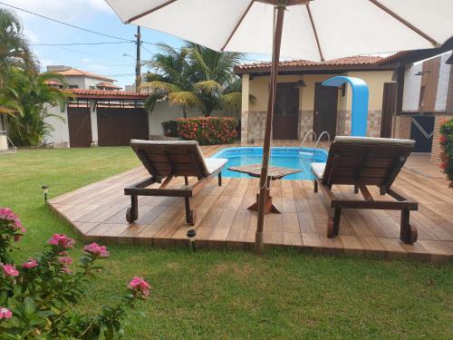 a patio with two chairs and an umbrella next to a pool at Porto Feliz in Barra de Jacuípe