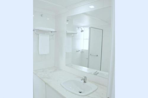 Baño blanco con lavabo y espejo en Hotel Vivendas Centro, en Erechim