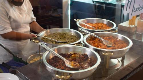 a woman standing in a kitchen preparing food in metal pots at Holiday Inn Queretaro Zona Krystal by IHG in Querétaro