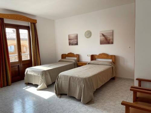 two beds in a room with a window at Hostal CAN GALLU in Cala Ratjada