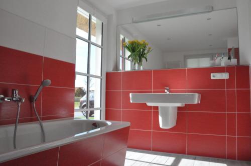 uma casa de banho vermelha com um lavatório e uma banheira em Ferienhaus Haubenlerche 63 - Haus Marilyn em Fuhlendorf