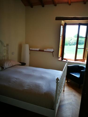 a bedroom with a bed and a window and a chair at Molino della Tuoma in San Quirico dʼOrcia