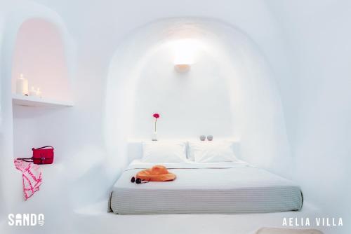a white bedroom with a bed with a orange towel on it at Traditional Cave Villas with Jacuzzi, Terrace and Sea view - Sando in Vourvoulos