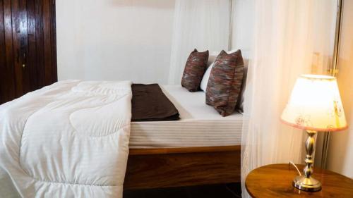 a bed with pillows and a lamp on a table at Upper Hill Place in Dar es Salaam