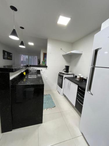 a kitchen with black counters and a white refrigerator at Le Bon Vivant - Praia Grande - Arraial do Cabo in Arraial do Cabo