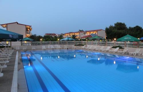 a large swimming pool with chairs and umbrellas at night at Ionion Beach Apartment Hotel & Spa in Arkoudi