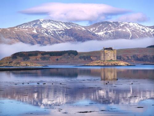 a castle on an island in a body of water with mountains at The Airds Hotel and Restaurant in Port Appin