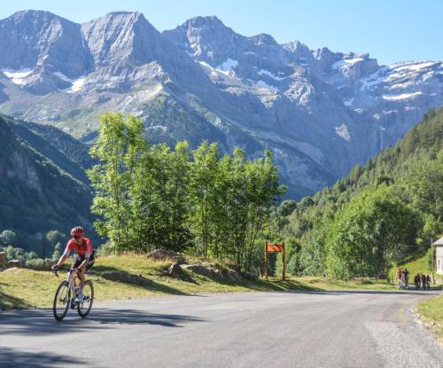 a man riding a bike down a road with mountains in the background at L'Argalyde Esprit Pyrénées Wellness & Cycling in Ayzac-Ost