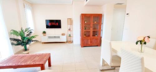 een woonkamer met een tafel en een tv aan de muur bij Apartamento Mediterráneo by DENIA COSTA in Denia