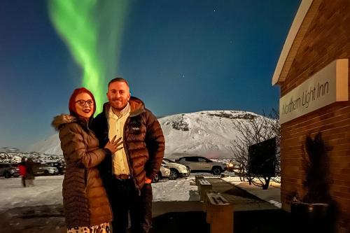 a man and a woman standing next to a building with green lights at Northern Light Inn in Grindavík