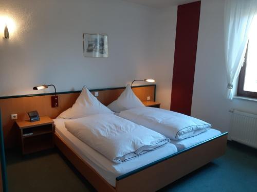 Schlafzimmer mit einem Bett mit weißer Bettwäsche und Kissen in der Unterkunft Hotel & Restaurant Eichholz in Kassel