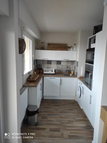 a kitchen with white cabinets and a wooden floor at Appartement de charme in Courseulles-sur-Mer