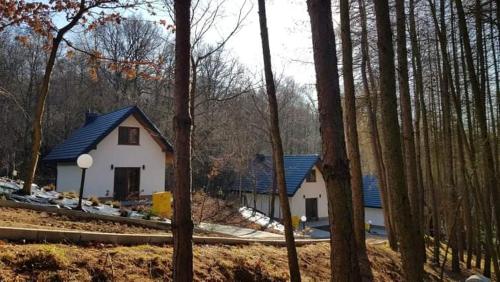a white house with a blue roof in the woods at Domki Łowisko Wieniec in Gdów