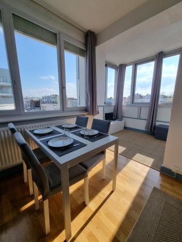 une salle à manger avec une table, des chaises et des fenêtres dans l'établissement Studio Malouin - Sur la digue de Malo les Bains avec vue sur mer, à Malo-les-Bains