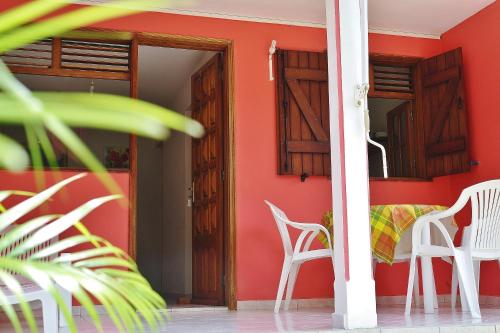 Cette chambre est dotée d'un mur rouge avec des chaises et une table. dans l'établissement Les Merveilleux Flots de la Mer, à Deshaies