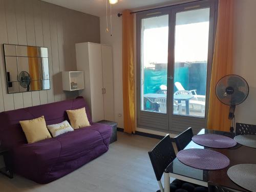 un salon avec un canapé violet et une table dans l'établissement Appartement Canet Sud Jardin et parking, à Canet