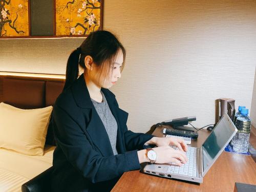 a woman sitting at a table using a laptop computer at Hotel Halrotto Fukuoka Hakata in Fukuoka