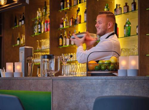 un homme debout derrière un bar avec un verre dans l'établissement Dorint Parkhotel Frankfurt / Bad Vilbel, à Bad Vilbel