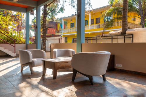 a patio with chairs and a table and a yellow building at juSTa Morjim Beach Resort Goa - 80 Steps from Morjim Beach in Morjim