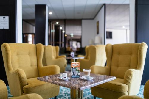 a waiting room with yellow chairs and a table with cups at Hotel Árpád in Tatabánya