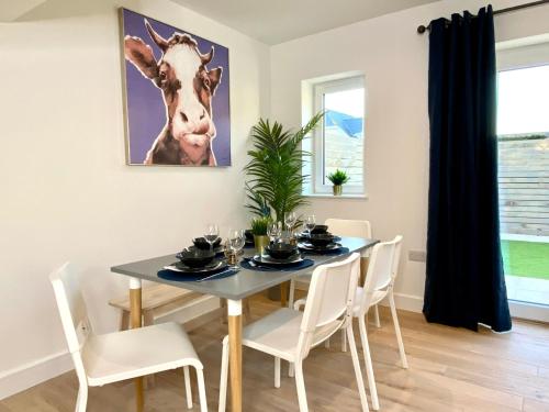 a dining room with a table with a cow picture on the wall at Amazing NEW Large 2 bedroom House - 5 Minutes to the nearest Beach! - Great Location - Garden - Parking - Fast WiFi - Smart TV - Newly decorated - sleeps up to 5! Close to Poole & Bournemouth & Sandbanks in Lytchett Minster