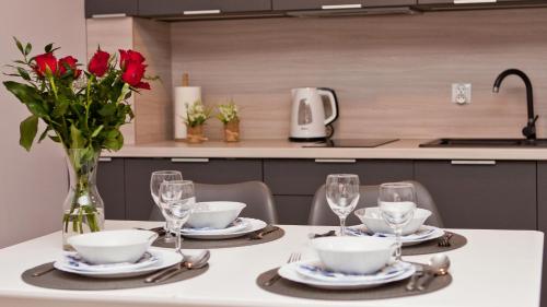 a table with a vase of red roses and glasses at Apartament Toscania in Kołobrzeg