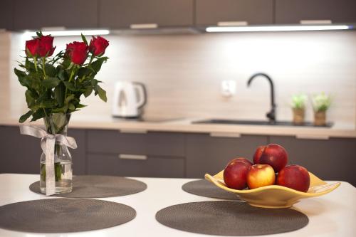 a table with a bowl of apples and a vase of roses at Apartament Toscania in Kołobrzeg