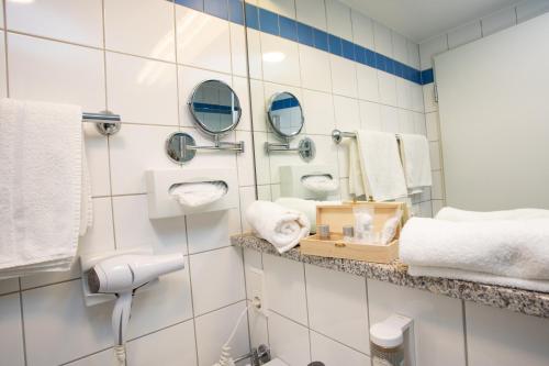 a bathroom with white tiled walls and mirrors at Hotel Hofgut Imsbach Lapointe in Tholey