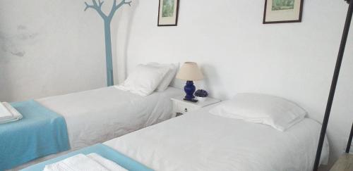 two beds in a white room with a lamp on a table at Casa do Páteo in Vila Nova da Baronia