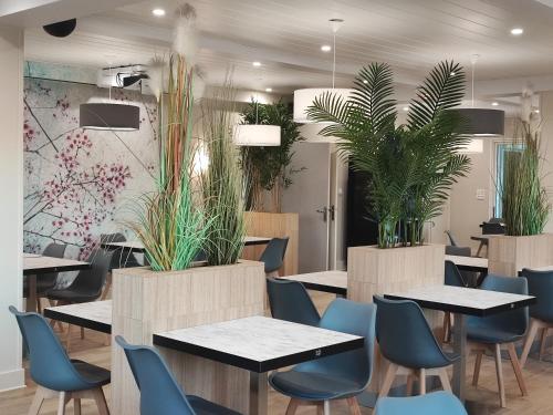 un restaurante con mesas, sillas y plantas en Le Relais des Primeurs LOGIS HOTEL, en Taulé