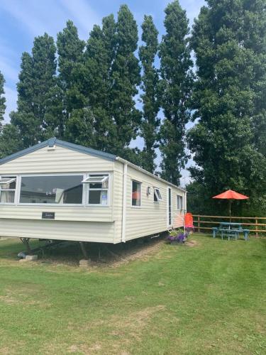 a white rv parked in a field next to trees at DaisyChain 2 Getaways - The perfect place to Stay - Play - Getaway in East Mersea