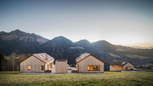 three wooden homes in a field with mountains in the background at Ferienhaus Bergfrieden Laterns auf 1.170 m in Laterns