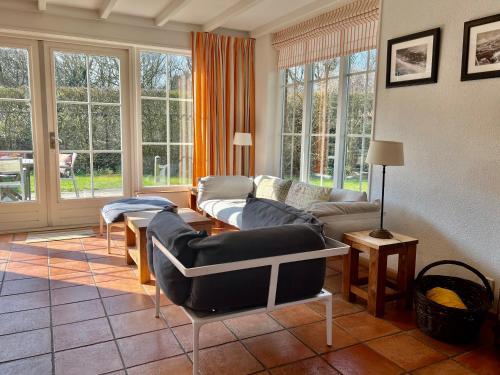 ein Wohnzimmer mit einem Sofa, Stühlen und Fenstern in der Unterkunft Uniek huis onderaan de duinen -veel privacy- eigen parkeerplaats in Domburg