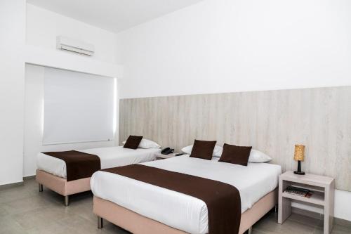 two beds in a hotel room with white walls at Hotel Palma Verde in Armenia