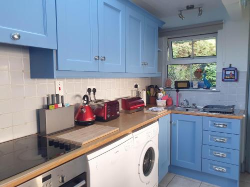a kitchen with blue cabinets and a washing machine at Idyllic Inchydoney Beach Cottage - Amazing sea views, path to beach! in Cork