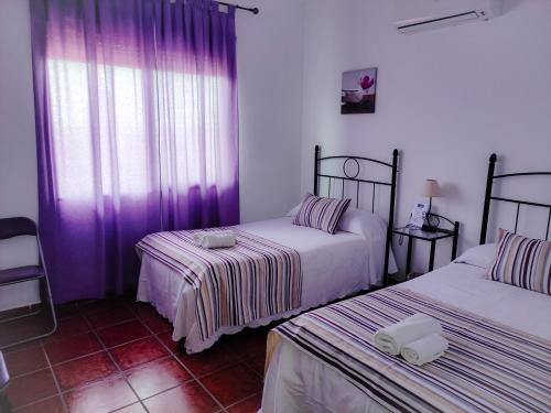 twee bedden in een kamer met paarse gordijnen en een kamer bij Casa Rural La Aduana in Villanueva del Fresno