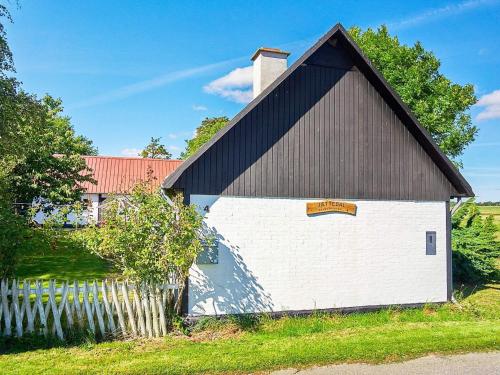een grote witte schuur met een zwart dak bij 5 person holiday home in Aakirkeby in Åkirkeby
