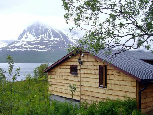una cabaña de madera con una montaña cubierta de nieve en el fondo en 5 person holiday home in Straumsbukta en Bakke