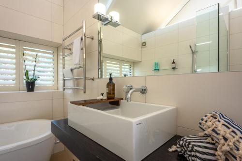a white bathroom with a sink and a bath tub at Waiheke Beachfront Apartment in Blackpool
