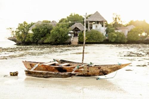a wooden boat sitting in the water in front of a house at The Island - Pongwe Lodge in Pongwe