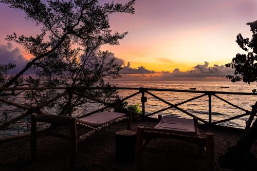 a sunset over the ocean with two chairs and a fence at The Island - Pongwe Lodge in Pongwe