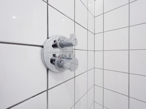 a white tiled wall with a shower valve at where to sleep in Copenhagen