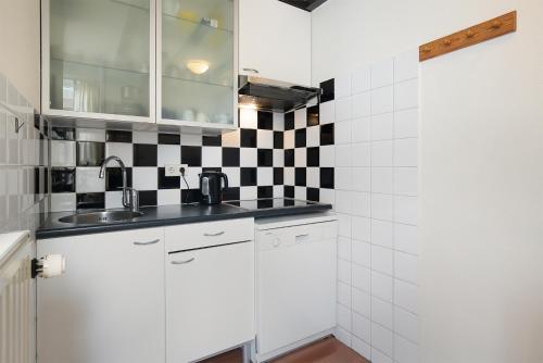 a kitchen with white cabinets and black and white tiles at Hello Zeeland - Vakantiehuis Beatrixstraat 27A in Domburg