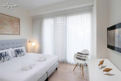 a white bedroom with a large bed and a chair at Dashing 1BR in White city by HolyGuest in Tel Aviv