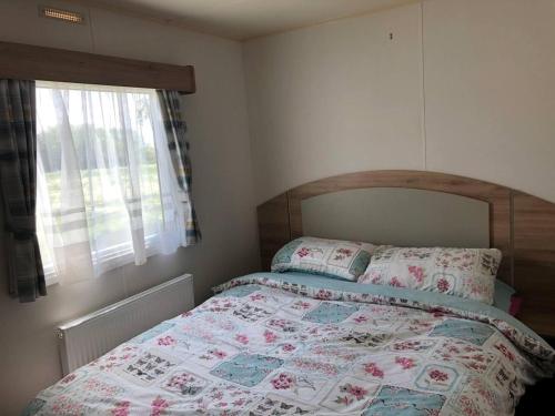 a bedroom with a bed with a floral quilt and a window at Lovely 3-Bed Caravan with Hot Tub in Lincolnshire in Lincoln