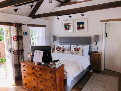 a bedroom with a bed and a wooden dresser with a laptop on it at The Old Dairy Retreat in St Austell