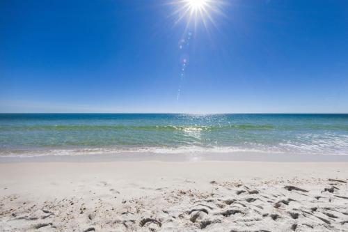 a sandy beach with the sun shining over the ocean at Tradewinds Unit 406 in Orange Beach