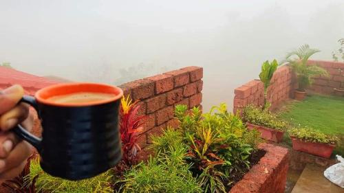 a person holding a coffee cup next to a brick wall at Redstone Hills, Diveagar in Diveagar